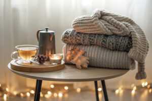 Cozy autumn composition with a cup of tea and a stack of knitted sweaters.